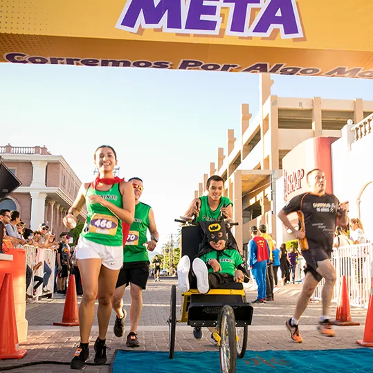 Corredores cruzando la meta de la carrera, uno de ellos en silla de ruedas adaptada